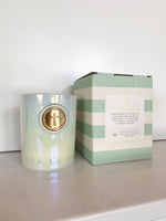 Iridescent candle with gold cross emblem next to a light green and white striped box