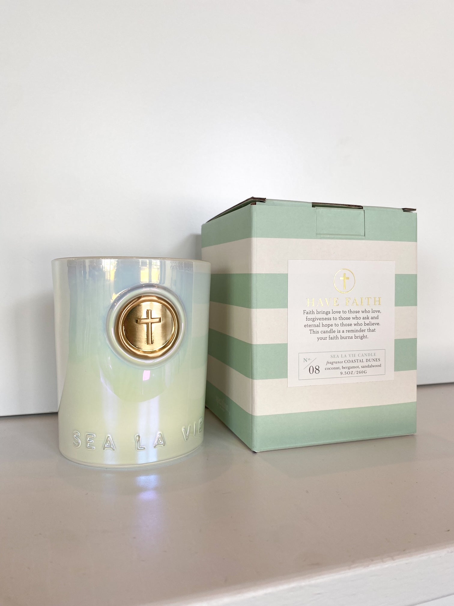 Iridescent candle with gold cross emblem next to a light green and white striped box