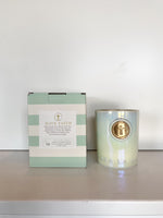 Sea La Vie Coastal Dunes candle and its striped packaging box with a gold cross emblem