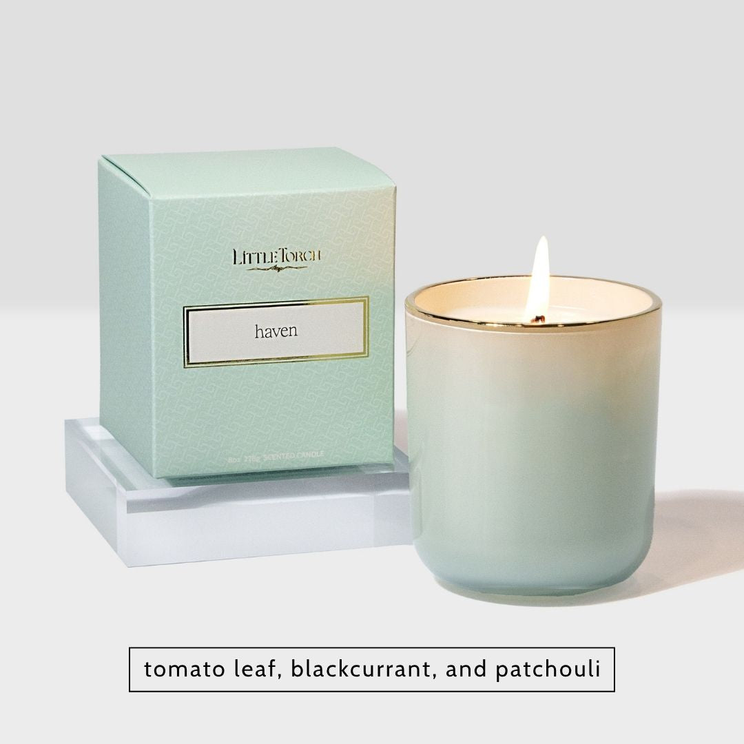 Little Torch Haven scented candle in a light green glass jar with a lit wick next to its matching box