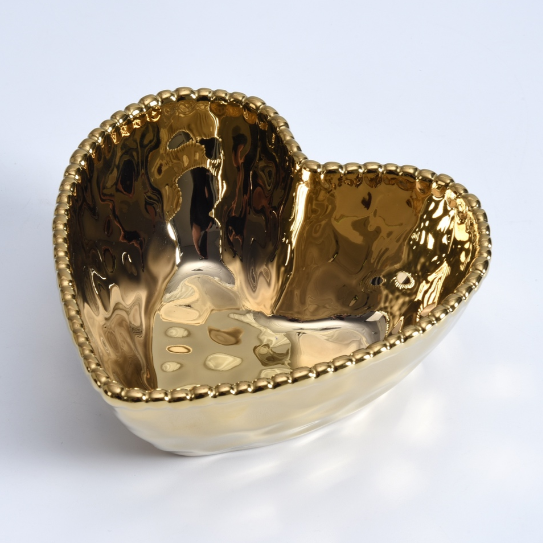 A gold heart-shaped bowl featuring a hammered, highly reflective interior and a decorative beaded rim on a white background