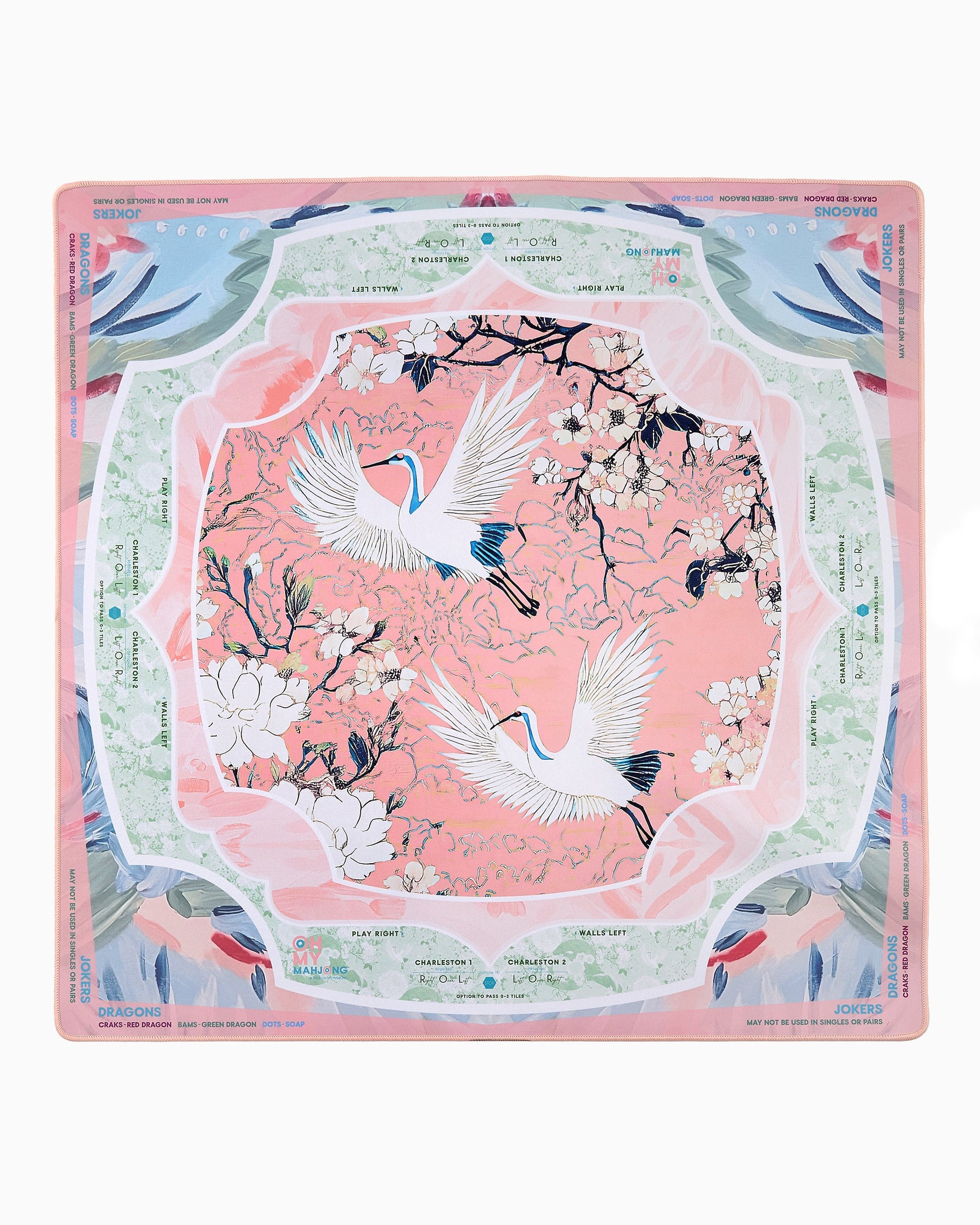 Oh My Mahjong printed mat featuring two white cranes with blue-tipped wings flying through white blossoms on a peach-pink background surrounded by mint green borders with Charleston gameplay instructions