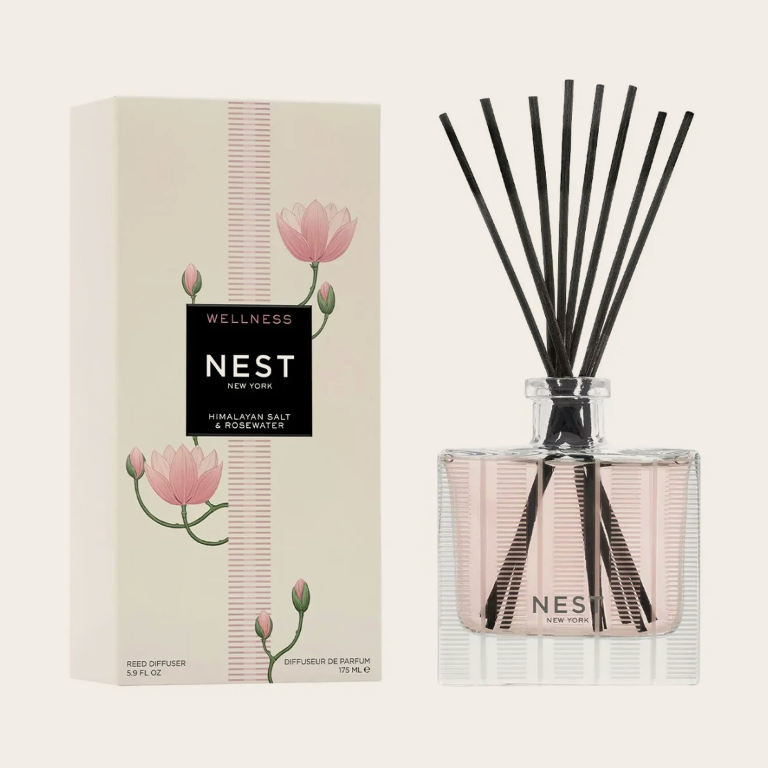 Product photo displaying a Nest New York Himalayan Salt & Rosewater reed diffuser set featuring an off-white box adorned with pink lotus flowers and a clear square glass bottle filled with pale pink liquid and black reeds