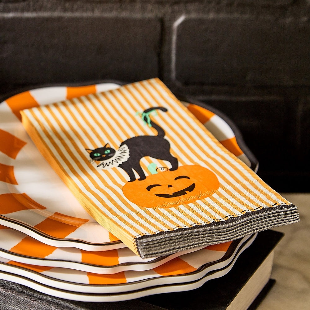 Halloween napkin with black cat and pumpkin illustration on stack of orange and white striped plates