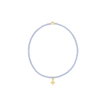 Handcrafted beaded jewelry featuring a circular periwinkle seed bead bracelet centered on a black background with a single polished gold bead and a petite gold cross charm