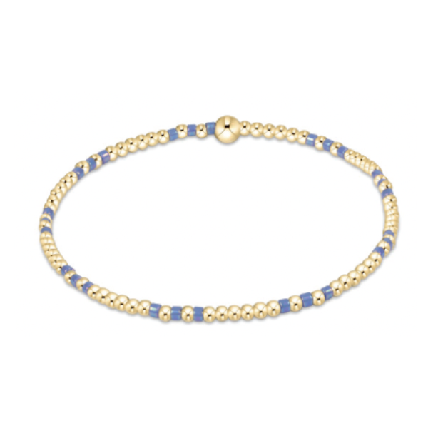 Delicate gold-tone beaded bracelet featuring small round beads interspersed with rectangular periwinkle blue beads and a central spherical gold bead