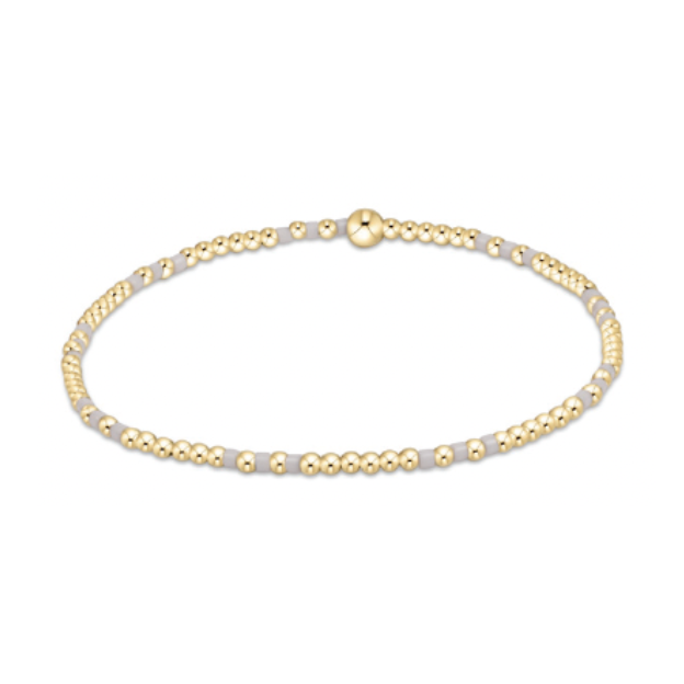 A delicate beaded bracelet featuring alternating tiny round gold beads and small flat light grey beads with a single larger gold bead as a focal point on a plain white background