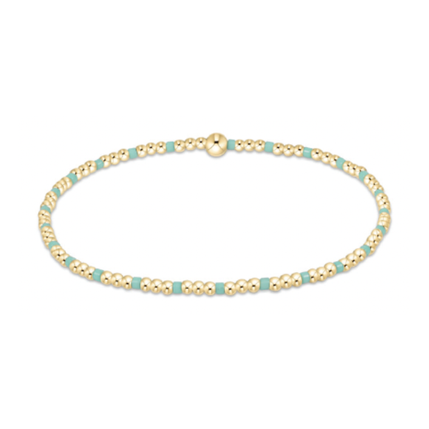 A thin gold beaded bracelet with intermittent small rectangular teal beads and a larger spherical gold bead