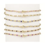 Six gold beaded bracelets with colorful accent beads and a central gold sphere bead on a white display