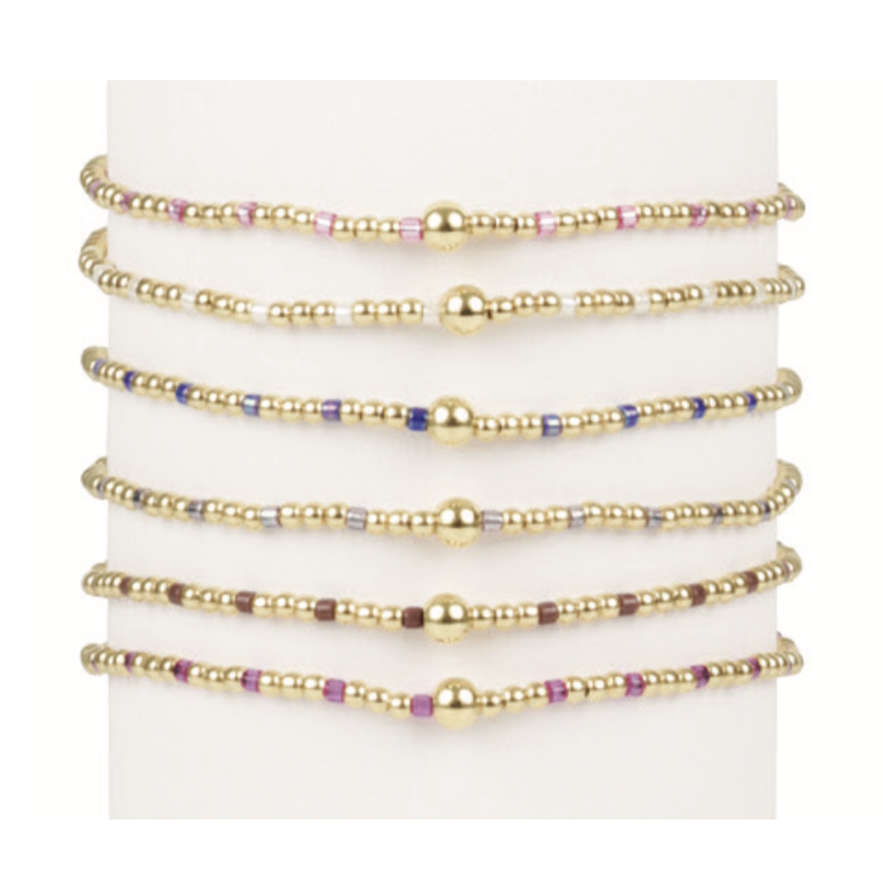 Six gold beaded bracelets with colorful accent beads and a central gold sphere bead on a white display