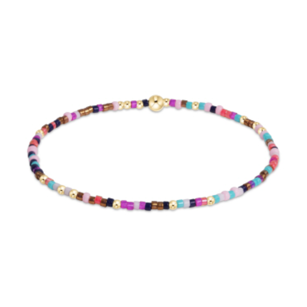 A delicate seed bead bracelet with a gold spherical clasp and small gold spacer beads featuring a vibrant mix of pink, purple, blue, and bronze hues