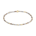 Beaded bracelet featuring tiny gold spacer beads interspersed with muted brown, grey, and cream cylindrical beads and a spherical gold clasp