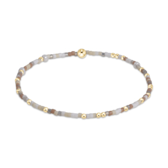 Beaded bracelet featuring tiny gold spacer beads interspersed with muted brown, grey, and cream cylindrical beads and a spherical gold clasp
