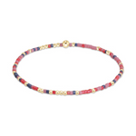 A delicate beaded bracelet featuring small gold spherical beads interspersed with colorful red, pink, and navy blue cylindrical seed beads