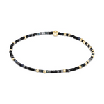 Delicate jewelry bracelet featuring tiny black, gray, and iridescent blue seed beads alternating with small gold-colored spacer beads and a central larger round gold bead