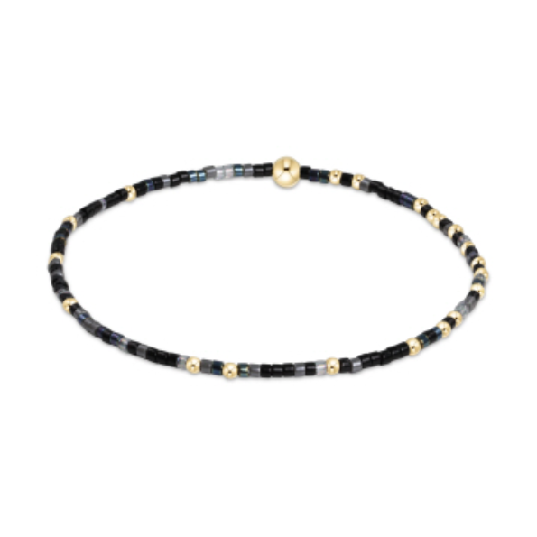 Delicate jewelry bracelet featuring tiny black, gray, and iridescent blue seed beads alternating with small gold-colored spacer beads and a central larger round gold bead