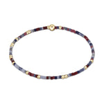 Delicate beaded bracelet featuring tiny square beads in red blue and grey colors accented by small round gold beads and a spherical gold clasp