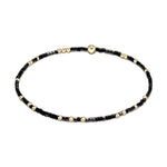 Jewelry: Delicate black and gold beaded bracelet featuring tiny seed beads, interspersed small round gold beads, and a central flat gold disc bead presented on a clean white background