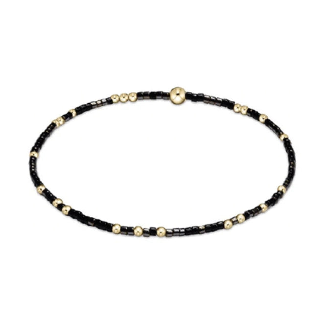 Jewelry: Delicate black and gold beaded bracelet featuring tiny seed beads, interspersed small round gold beads, and a central flat gold disc bead presented on a clean white background