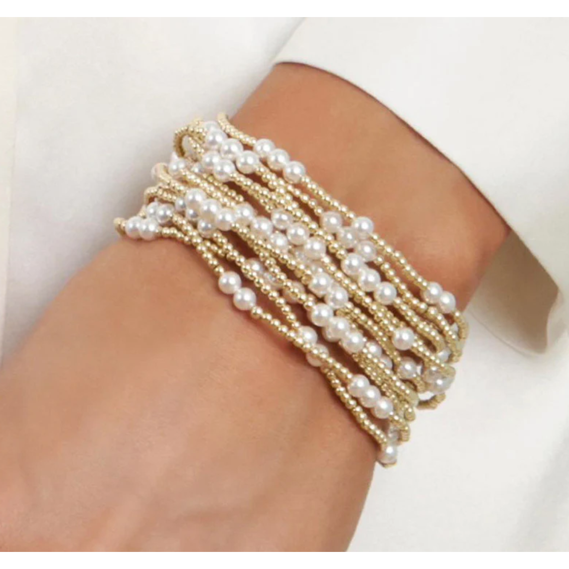Multi strand bracelet with gold beads and white pearls on a wrist