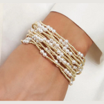 Photograph of a multi-strand bracelet made of luminous white pearls and tiny shimmering gold beads worn elegantly on a wrist against a crisp white shirt cuff