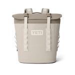 Product image of a two-tone beige and tan Yeti Hopper M20 Soft Cooler Backpack featuring a prominent Yeti logo, white buckle straps securing the roll-top closure, and padded shoulder straps