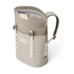Product photography of a tan and cream YETI Hopper M12 backpack soft cooler with a magnetic MagShield Access top opening and white attachment webbing on a black background