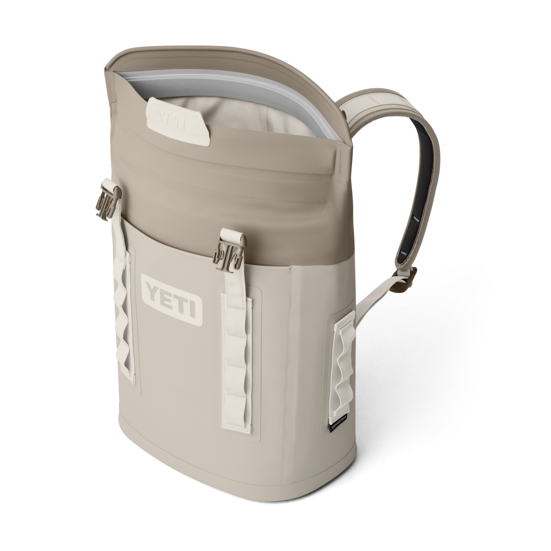 Product photography of a tan and cream YETI Hopper M12 backpack soft cooler with a magnetic MagShield Access top opening and white attachment webbing on a black background
