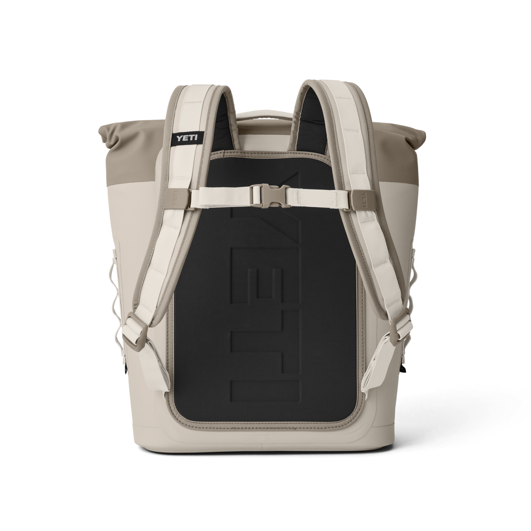 Yeti product photo of a two-tone tan and taupe roll-top backpack cooler on a black background, featuring white padded shoulder straps, a chest buckle, and an embossed Yeti logo on the black back panel