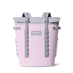 Digital product photograph of a light pink YETI backpack cooler featuring a gray roll-top closure two gray buckle straps and a prominent YETI logo centered on the front presented on a black background