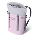 A light pink and grey YETI Hopper M20 backpack cooler with an open magnetic top and side attachment straps, presented on a black background