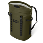 Product photography by YETI of an olive green cooler backpack isolated on a black background featuring a prominent YETI logo black strap details and an open roll-top with white interior