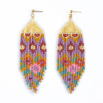 Pair of handcrafted seed bead fringe earrings on white featuring gold-tone stud tops and a geometric pattern in lavender, mustard yellow, teal, and pink