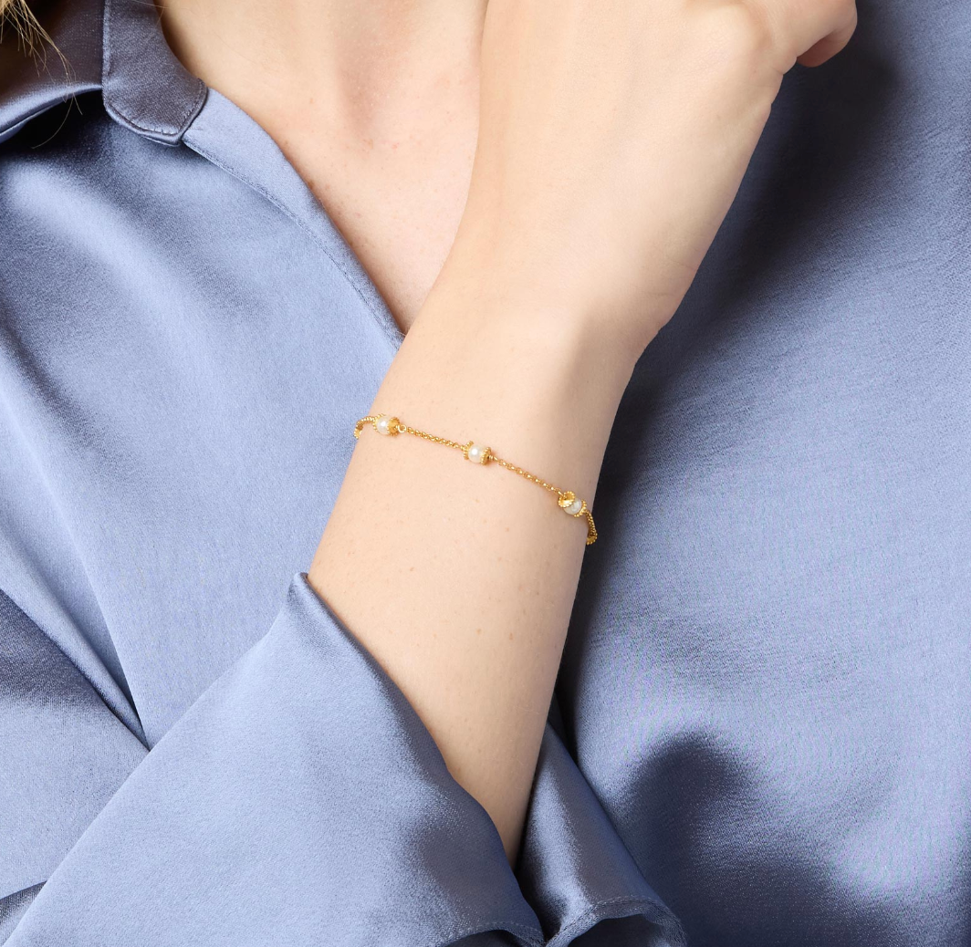 Gold chain bracelet with small white pearls worn on a wrist