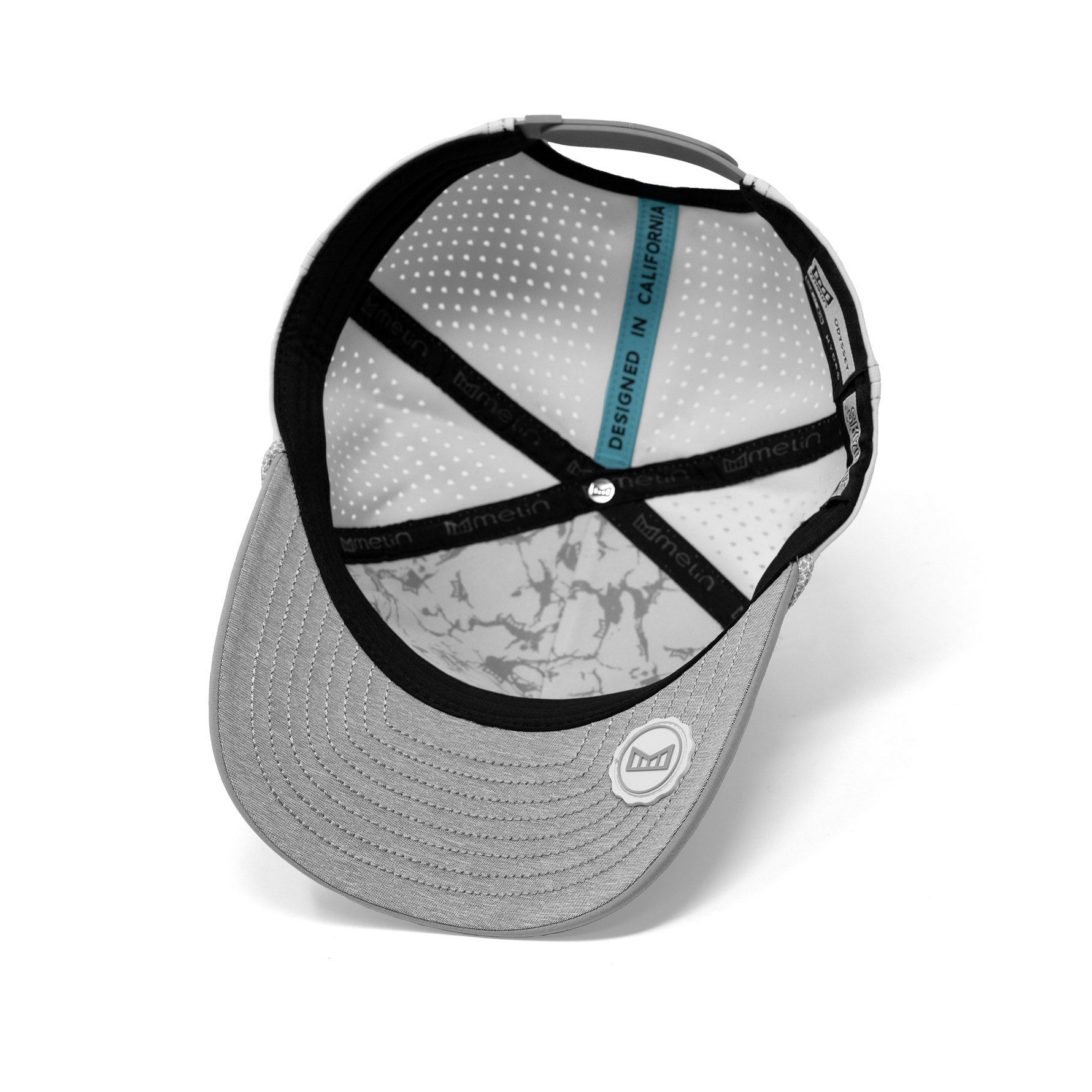 Grey Melin snapback cap featuring a perforated white interior with a subtle grey marble pattern, black branded crisscross straps, a blue 'DESIGNED IN CALIFORNIA' tag, and a textured brim with a white rubberized Melin logo