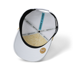 Product photo Melin white cap interior displaying a perforated crown gold geometric patterned brim underside and a light blue DESIGNED IN CALIFORNIA tag