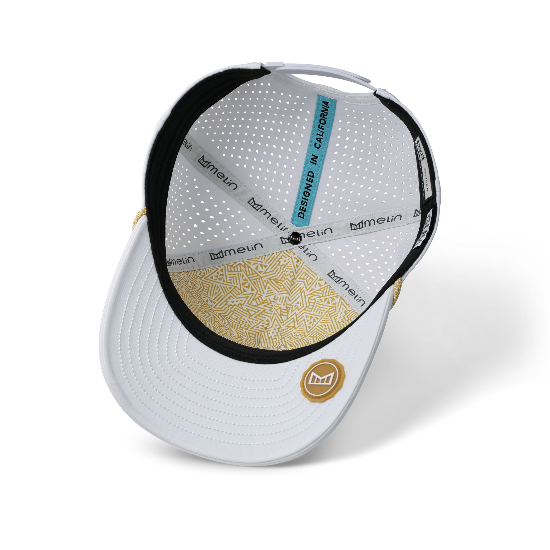 Product photo Melin white cap interior displaying a perforated crown gold geometric patterned brim underside and a light blue DESIGNED IN CALIFORNIA tag