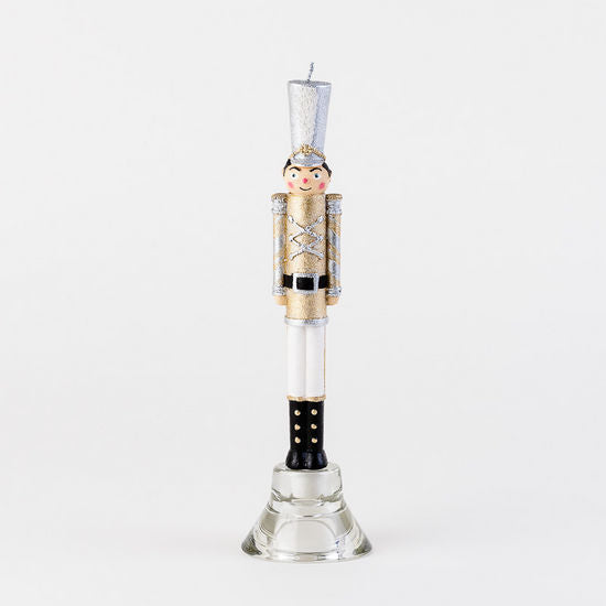 Nutcracker shaped taper candle in gold and silver uniform on a glass stand