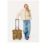 Woman wearing a cream puffer jacket and blue jeans standing next to an olive green rolling tote bag