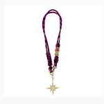 A designer lanyard with a braided pink and black patterned cord, featuring gold and pink beaded embellishments, and a sparkling gold starburst pendant adorned with pave diamonds