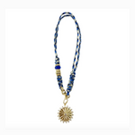 A blue white and black braided cord lanyard featuring a dark blue bead a gold-tone textured bead and a gold sunburst pendant with a central clear gem and surrounding small gems