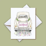 Illustration of a white vintage wedding car with a pink "Just Married" sign adorned with green leaves and small pink flowers, trailing colorful bottles and hearts from the bumper, presented as a greeting card on a light green background