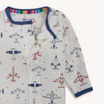 Textile, eco-friendly me brand, a baby's long-sleeved sleeper featuring a white background with a vibrant pattern of various red, blue, and yellow airplanes and scattered stars, finished with blue collar piping and a rainbow striped inner collar