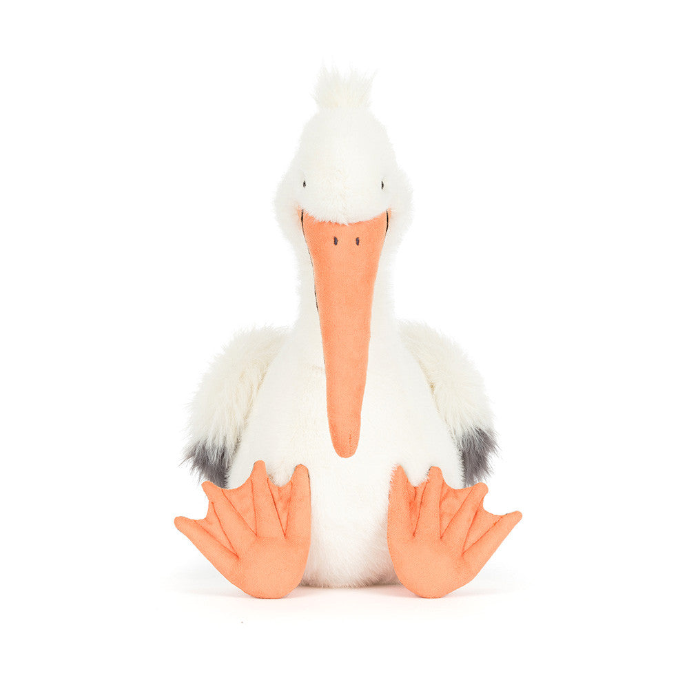 Plush toy by Jellycat of a white pelican sitting against a plain white background featuring a long peach-colored beak, oversized orange webbed feet, and charcoal grey-tipped wings