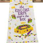 White cotton kitchen towel with a Mardi Gras King Cake design in purple, green, and gold, showing a king cake, slices, crowns, a king cake baby, confetti, and the text the KING CAKE KNIFE stays in the BOX