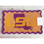 Coir doormat by Mary Square featuring a large purple and gold LSU logo with a wavy scalloped border on a light wood floor