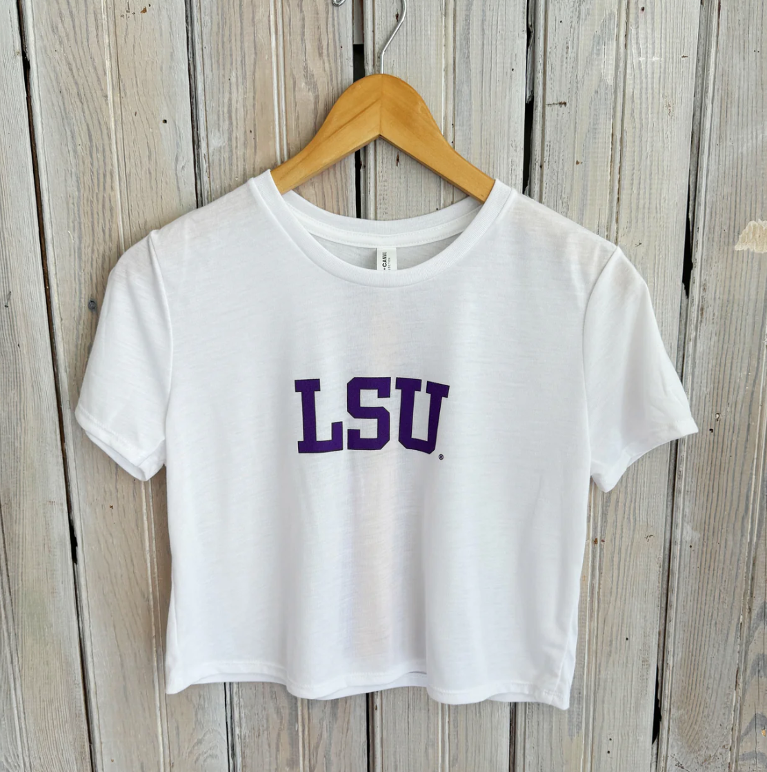 White short sleeve crop top with purple LSU lettering on a wooden hanger