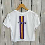 White cropped t-shirt featuring purple and gold vertical stripes with 'TIGERS' text, hanging on a wooden hanger against a weathered white wooden wall