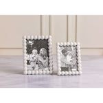 Product photograph featuring two white beaded Mud Pie photo frames, one larger and one smaller, each holding a black and white image of a happy family with a baby, displayed on a smooth light gray marble countertop