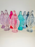 Group of translucent colored glass statues of the Virgin Mary on a white surface